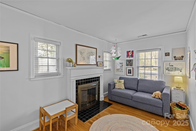 living room with a tiled fireplace, wood finished floors, visible vents, and crown molding