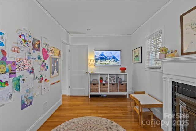 interior space featuring baseboards, a tiled fireplace, wood finished floors, and crown molding