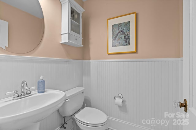 half bathroom with a wainscoted wall, a sink, and toilet