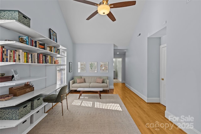 living area with visible vents, light wood-style floors, ceiling fan, high vaulted ceiling, and baseboards