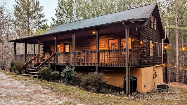 log home featuring cooling unit, covered porch, roof with shingles, and log siding