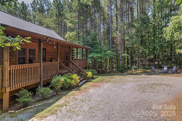 view of yard with a porch, driveway, and a view of trees