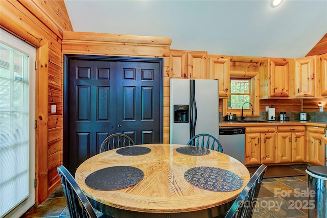 kitchen with stone tile floors, a sink, vaulted ceiling, dishwasher, and stainless steel fridge