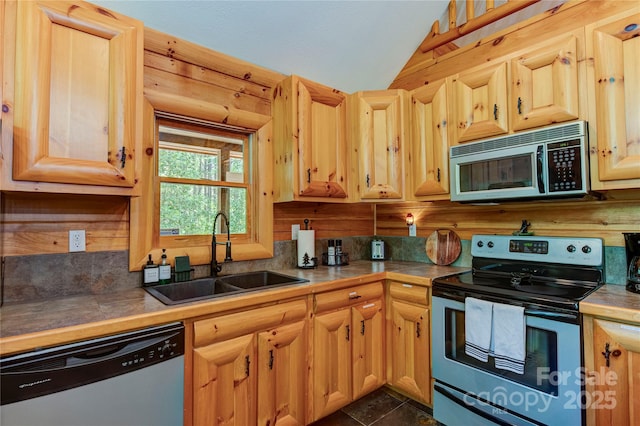 kitchen featuring light brown cabinets, appliances with stainless steel finishes, vaulted ceiling, and a sink