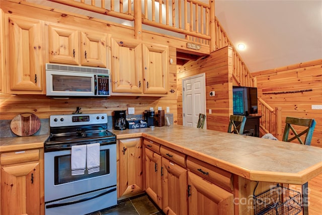 kitchen with a peninsula, wooden walls, stainless steel appliances, and tile countertops