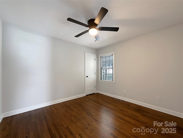 spare room featuring a ceiling fan, visible vents, dark wood finished floors, and baseboards