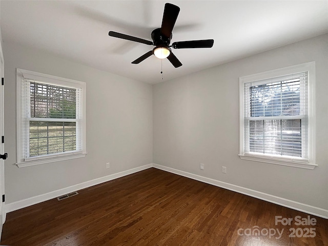 empty room with dark wood-type flooring, plenty of natural light, visible vents, and baseboards