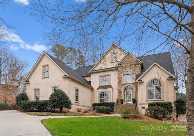 french country inspired facade featuring stucco siding, roof with shingles, and a front yard