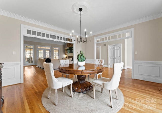 dining space with a notable chandelier, wainscoting, crown molding, and light wood-type flooring