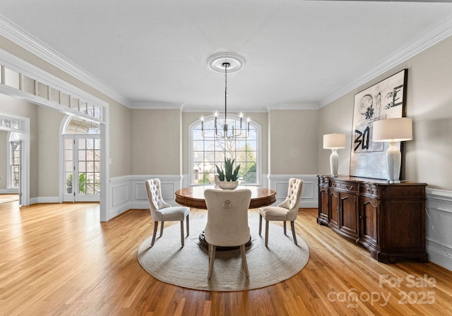 dining room featuring an inviting chandelier, wainscoting, crown molding, and light wood finished floors