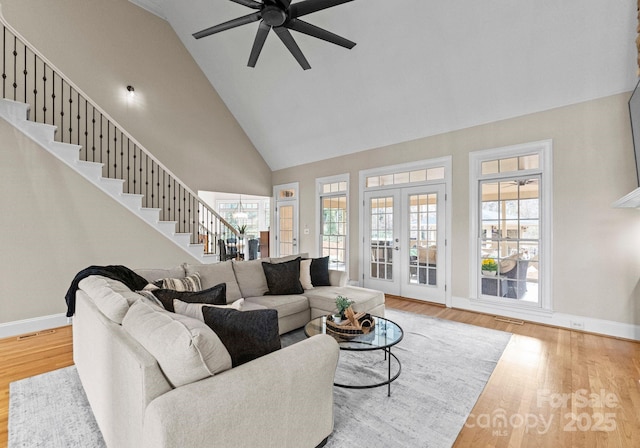 living area with wood finished floors, high vaulted ceiling, ceiling fan, stairs, and french doors