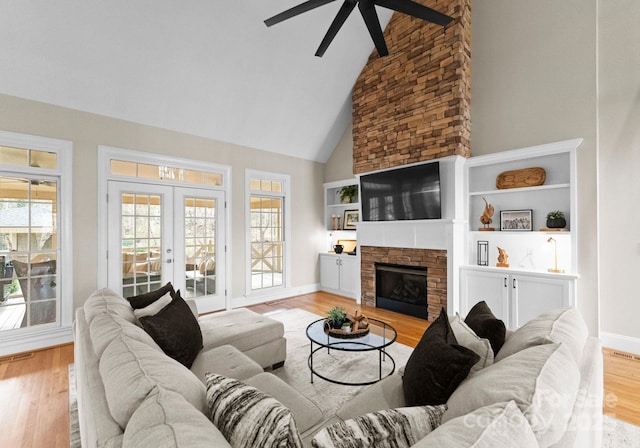 living room with ceiling fan, a stone fireplace, french doors, wood finished floors, and high vaulted ceiling