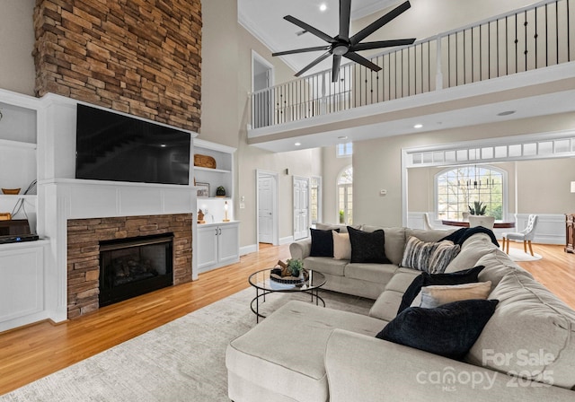 living area featuring built in shelves, light wood-style flooring, a fireplace, crown molding, and ceiling fan