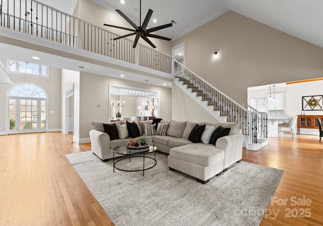 living area with stairway, baseboards, ornamental molding, ceiling fan, and light wood-style floors