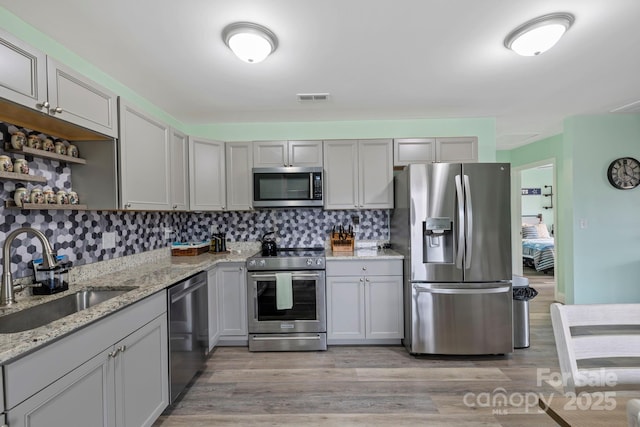 kitchen with visible vents, backsplash, light wood-style floors, stainless steel appliances, and a sink