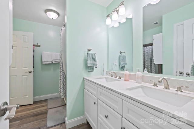 bathroom with double vanity, wood finished floors, baseboards, and a sink