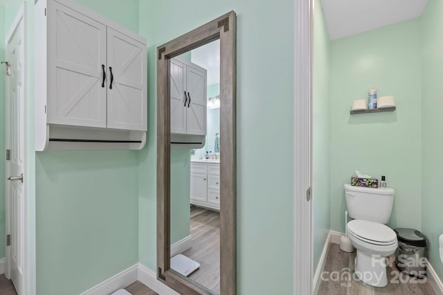 bathroom with toilet, vanity, baseboards, and wood finished floors