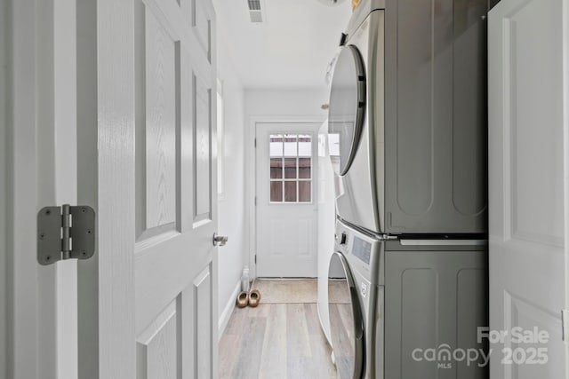 clothes washing area with stacked washer / drying machine, light wood-style floors, visible vents, and laundry area