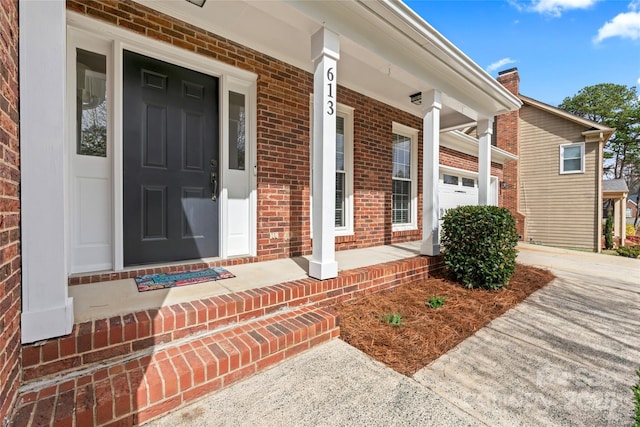 view of exterior entry with a garage, driveway, brick siding, and a porch