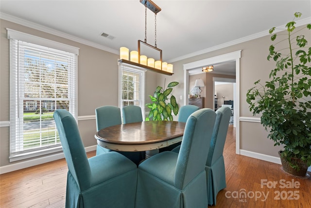 dining area featuring light wood-style floors, visible vents, crown molding, and baseboards