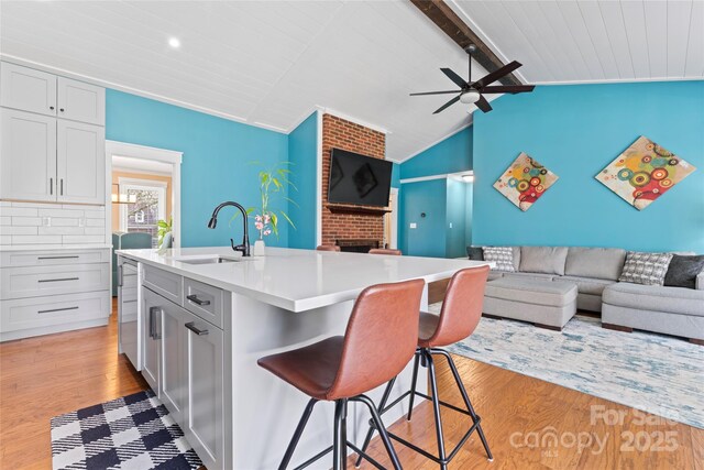 kitchen featuring a breakfast bar area, open floor plan, vaulted ceiling with beams, light wood-type flooring, and a sink