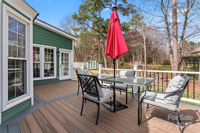 wooden terrace with fence, a storage unit, outdoor dining area, and an outdoor structure