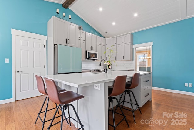 kitchen featuring decorative backsplash, lofted ceiling with beams, freestanding refrigerator, light wood-type flooring, and a sink