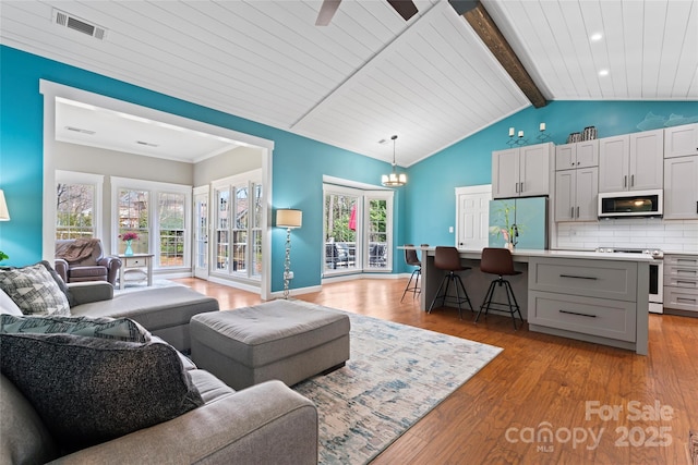 living room with visible vents, baseboards, lofted ceiling with beams, an inviting chandelier, and light wood-type flooring