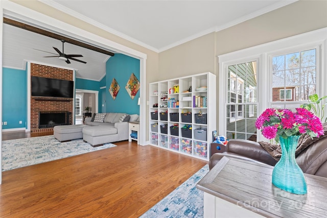 living area with lofted ceiling, ceiling fan, wood finished floors, crown molding, and a fireplace