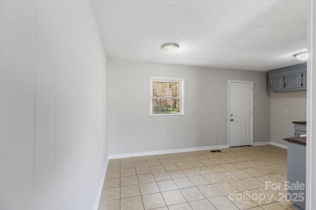 unfurnished room featuring light tile patterned flooring, visible vents, a textured ceiling, and baseboards