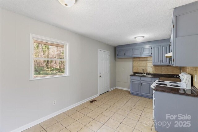 kitchen with dark countertops, backsplash, under cabinet range hood, electric stove, and a sink