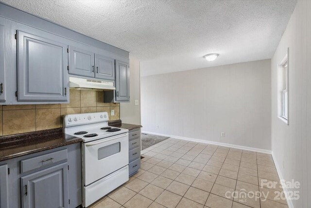 kitchen featuring gray cabinets, under cabinet range hood, tasteful backsplash, dark countertops, and white electric range oven