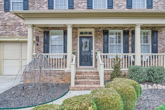 doorway to property with a garage, brick siding, and covered porch