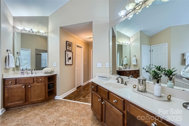 bathroom with tile patterned floors, lofted ceiling, two vanities, a sink, and baseboards