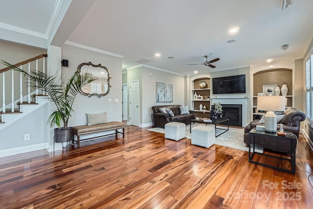 living room with wood finished floors, stairway, a fireplace, baseboards, and ceiling fan