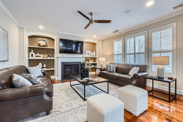 living area with crown molding, a fireplace with flush hearth, wood finished floors, and visible vents