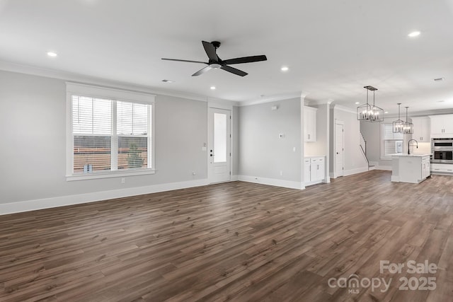 unfurnished living room featuring dark wood-style floors, ceiling fan with notable chandelier, a sink, and ornamental molding