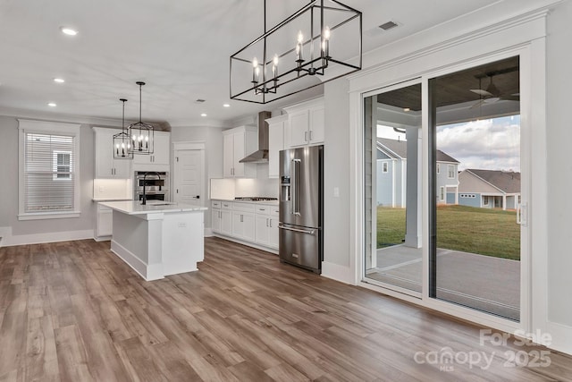 kitchen featuring light countertops, appliances with stainless steel finishes, wall chimney range hood, and white cabinetry