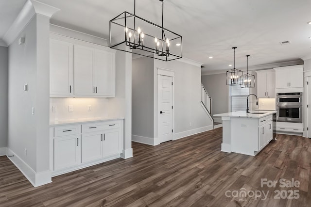 kitchen with crown molding, light countertops, double oven, white cabinets, and a sink