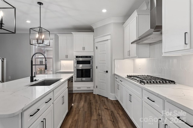 kitchen featuring white cabinets, decorative backsplash, stainless steel appliances, wall chimney range hood, and a sink