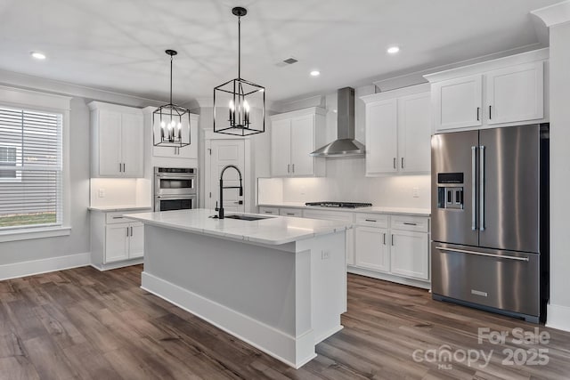 kitchen with a sink, appliances with stainless steel finishes, wall chimney range hood, and white cabinetry