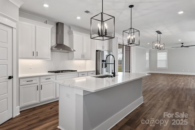 kitchen featuring visible vents, wall chimney exhaust hood, appliances with stainless steel finishes, a kitchen island with sink, and a sink