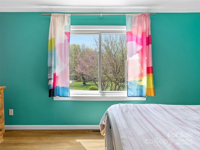 bedroom featuring multiple windows, baseboards, ornamental molding, and wood finished floors