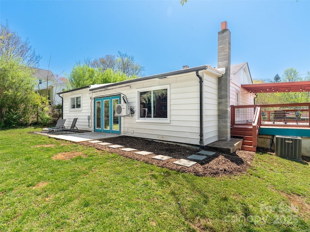 rear view of property featuring a lawn, a chimney, central air condition unit, french doors, and a wooden deck