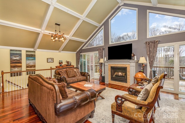 living room with a chandelier, beamed ceiling, a warm lit fireplace, and wood finished floors