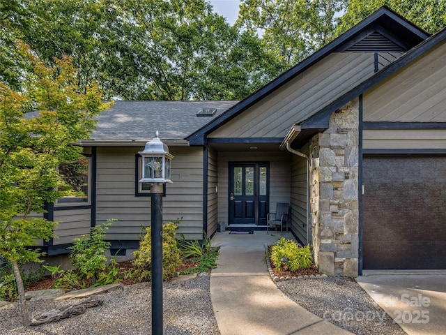 doorway to property with a garage, stone siding, and roof with shingles