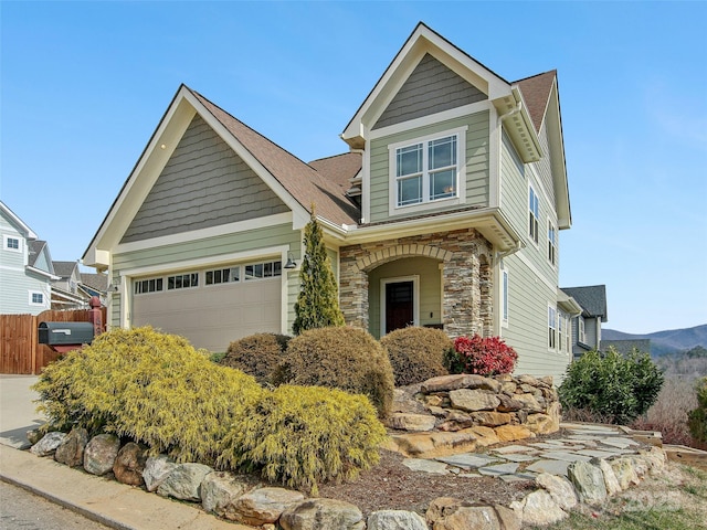 craftsman-style house with an attached garage, stone siding, and fence