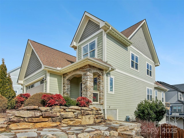 view of side of property with a garage, stone siding, and a shingled roof