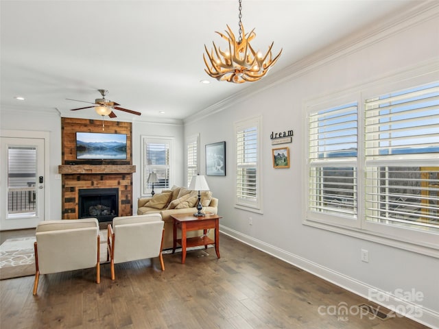 living area with ceiling fan with notable chandelier, a fireplace, baseboards, ornamental molding, and dark wood-style floors