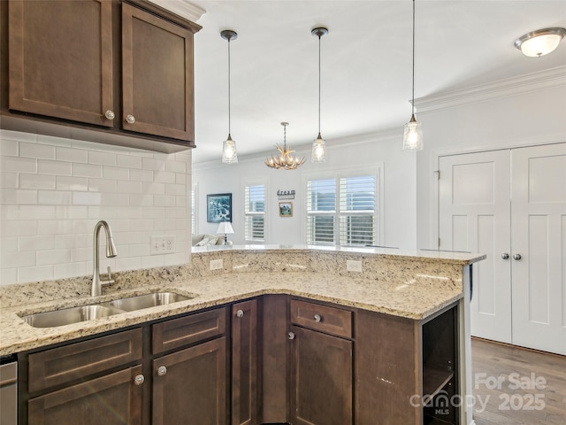 kitchen featuring a peninsula, ornamental molding, a sink, and dark brown cabinets